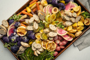 sheet pan of roasted spring vegetables topped with sliced chicken sausage that has been grilled