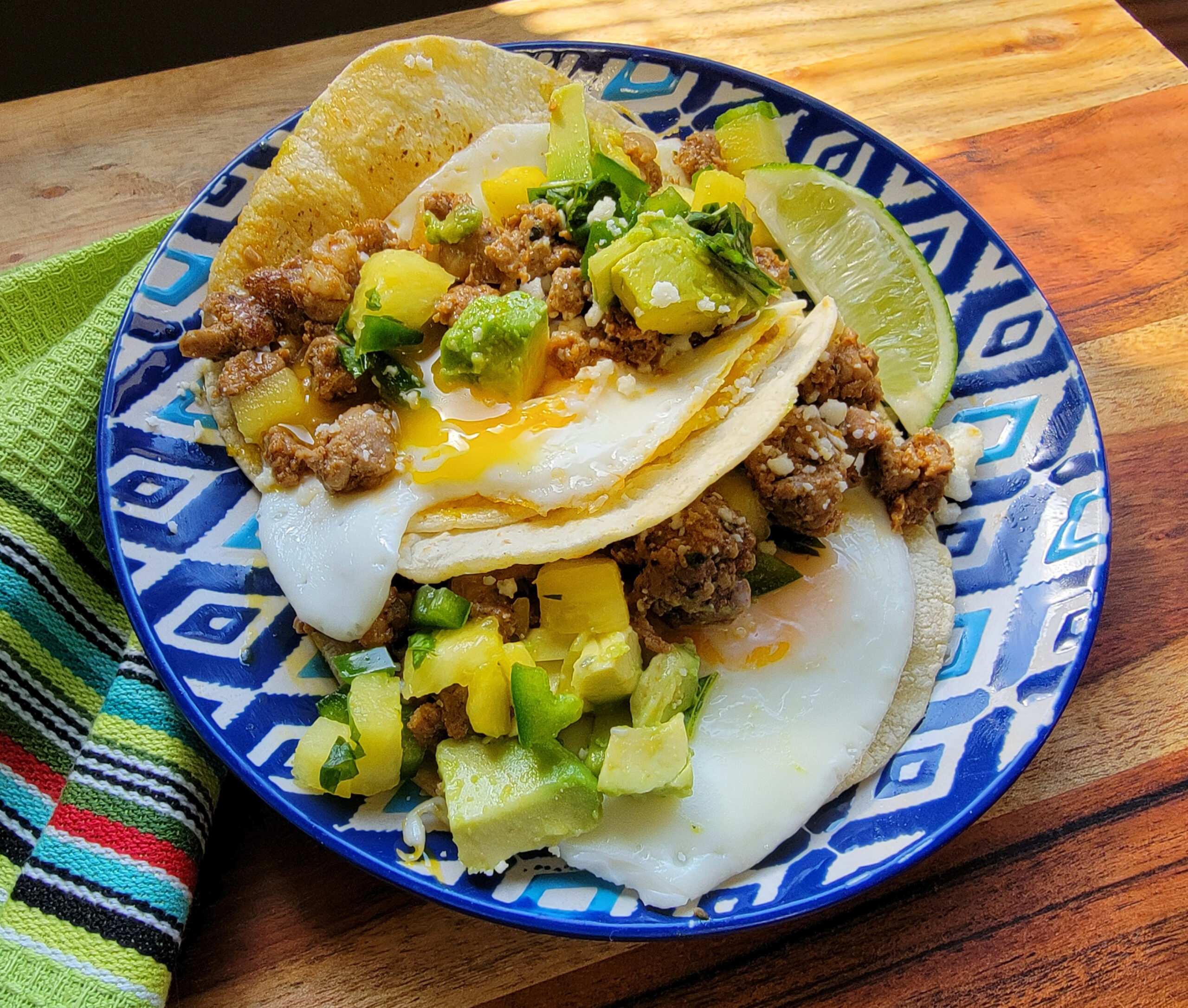 Blue plate with breakfast tacos that have Isernio's Al Pastor, eggs, and avocado.