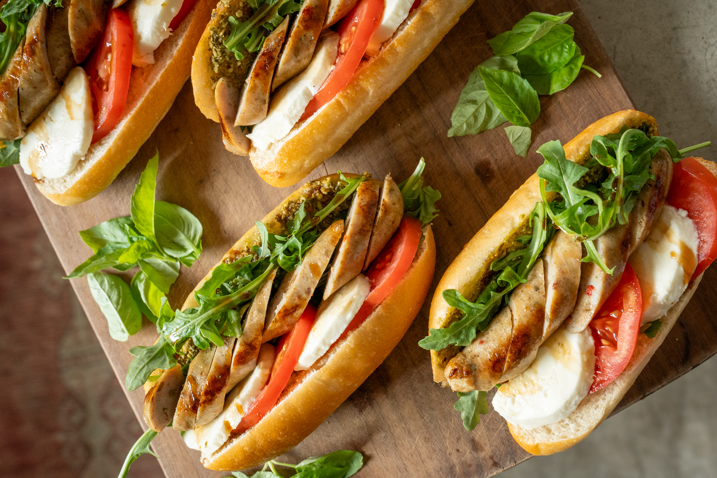 four hoagie sandwich rolls filled with sliced chicken sausage, tomatoes, fresh basil and mozzarella