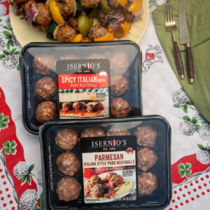Packaged Isernio's meatballs on a table. A tray of meatball and vegetable kebabs behind the tray.