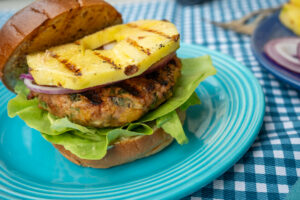 Blue plate with a grilled Isernio's chicken burger and pineapple between a bun.