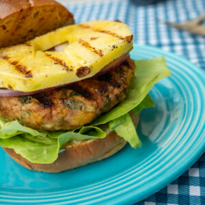 Blue plate with a grilled Isernio's chicken burger and pineapple between a bun.