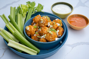 Isernio's chicken meatballs cooked in Buffalo sauce served in a blue bowl with blue cheese and celery sticks.