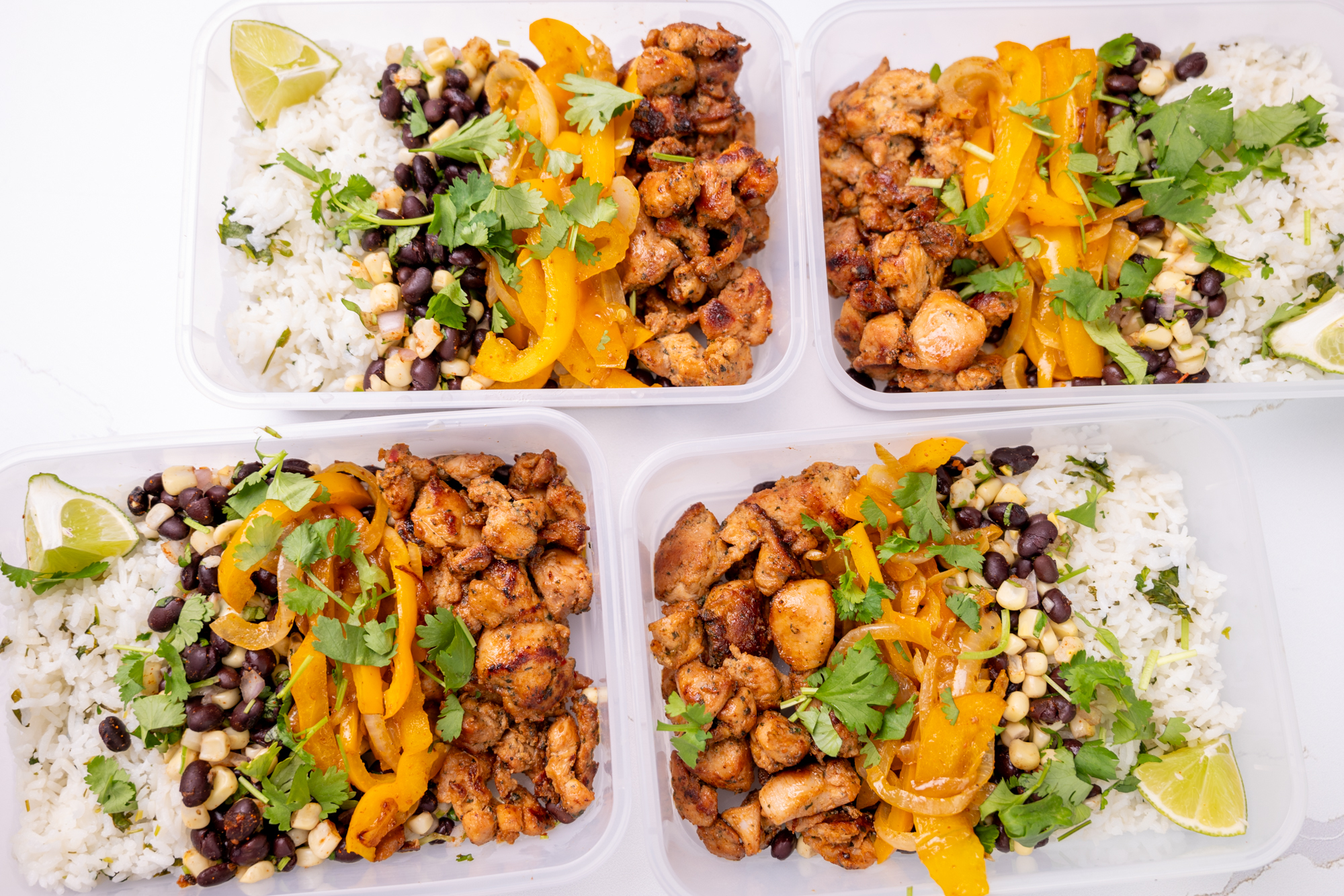 Meal preparation of four Tupperwares filled with Isernio's marinated chicken thighs, black beans, cilantro-lime rice and cooked bell peppers.