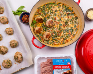 A sheetpan with Isernio's ground chicken meatballs that have been baked and feature a tomato cream sauce on the side.